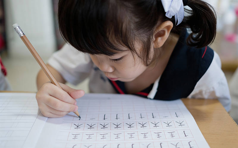 Child learning Chinese by practicing character strokes in workbook