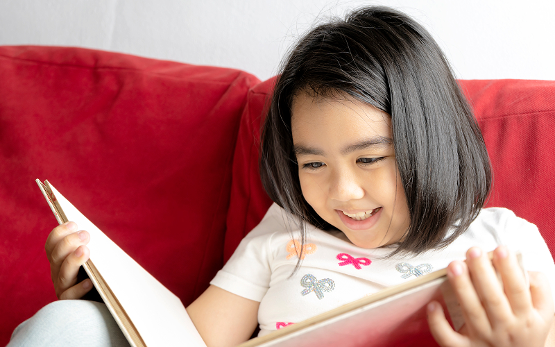 Happy girl reading a book to practice Chinese language skills.