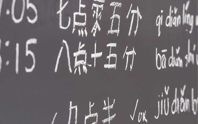 Blackboard with Chinese pinyin and characters for grammar practice.