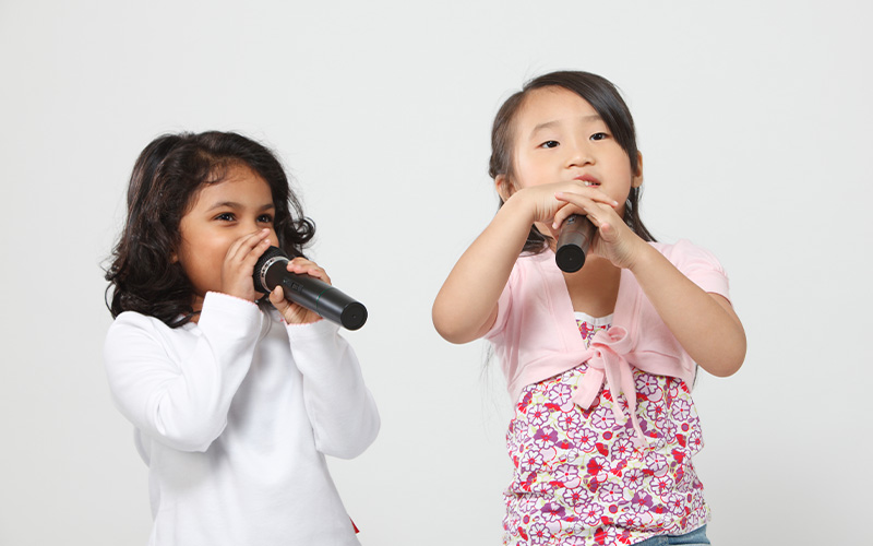 Two young girls happily singing into microphones during a Chinese language performance.