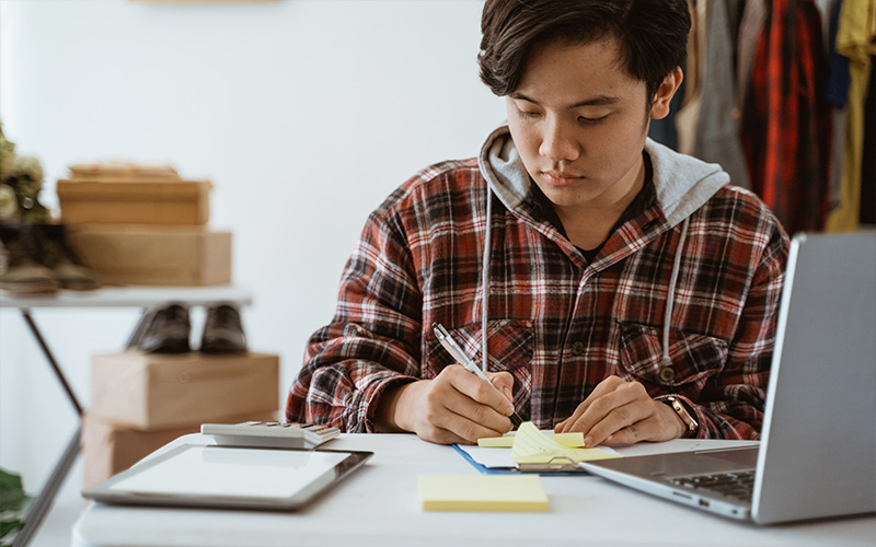 A focused student wearing a flannel shirt is writing on a paper
